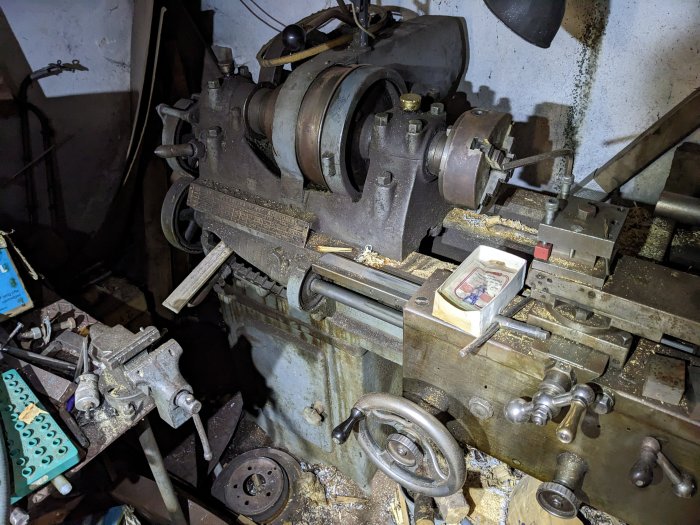 Äldre metallbearbetningsmaskin, förmodligen en svarv, i arbetsmiljö med damm och verktyg.