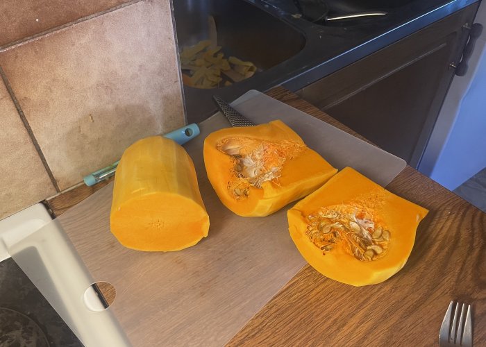 Uppskuret butternutpumpa på skärbräda, kniv, gaffel, köksbänk, skärbrädas hål.