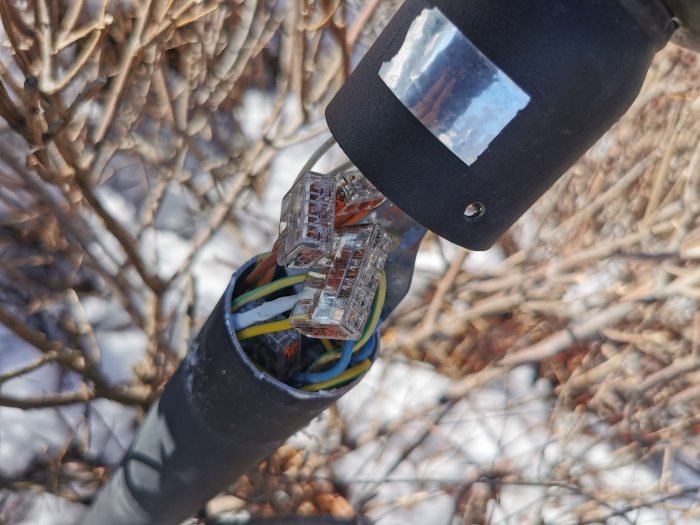 Elledningar anslutna till kontakter i stolpe, utomhus, dagtid, snö, bar kvistbakgrund.