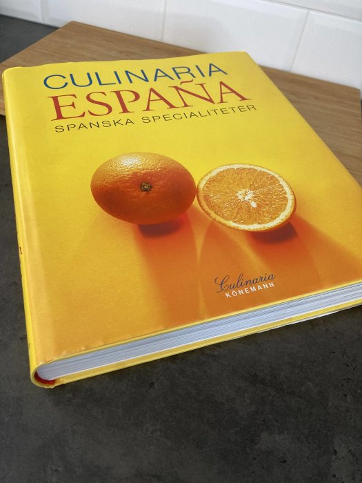 En kokbok med titeln "CULINARIA ESPAÑA", och en hel och en halverad apelsin ovanpå.