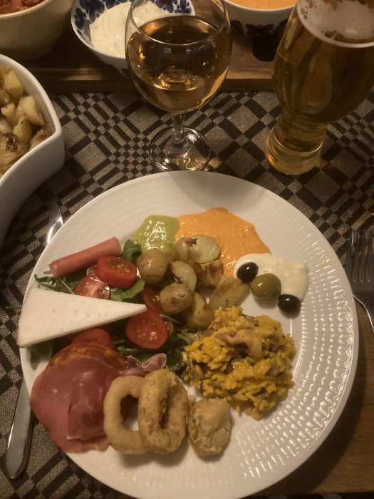 Ett dukat bord med blandad mat, öl och vin, för en måltid. Rostade potatisar, sallad, kallskuret, friterade ringar, risrätt.