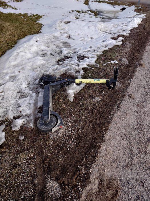 En övergiven elsparkcykel ligger på en smutsig snökantrandad mark.