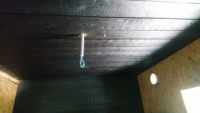 Mörkt trätak med möjlig trädkoja-känsla, spiralfjäder och krok med blått snöre hänger ner.