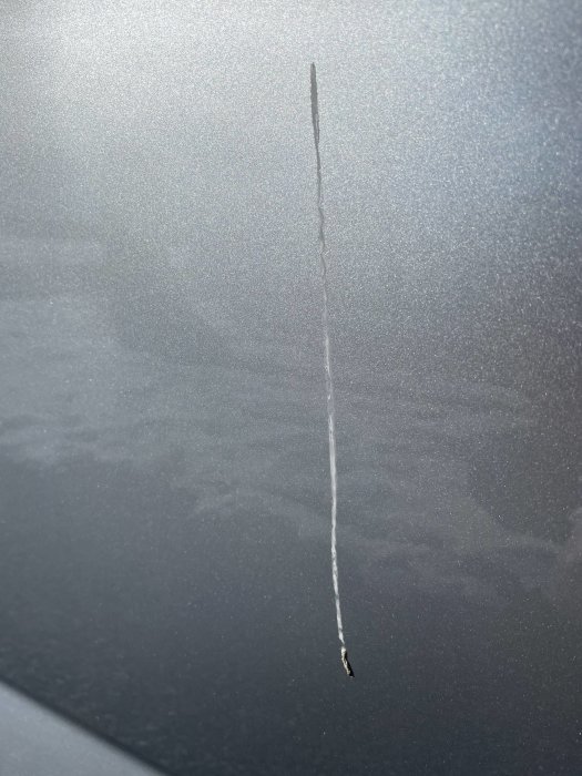 En repa på en blank, mörkgrå yta, möjligen en bil, med en oskarp reflektion.