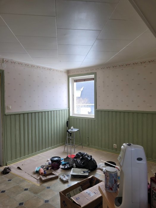 Ett rum under renovering med målarutrustning, tapetsering gjord halvvägs och materialet utspridd på golvet.