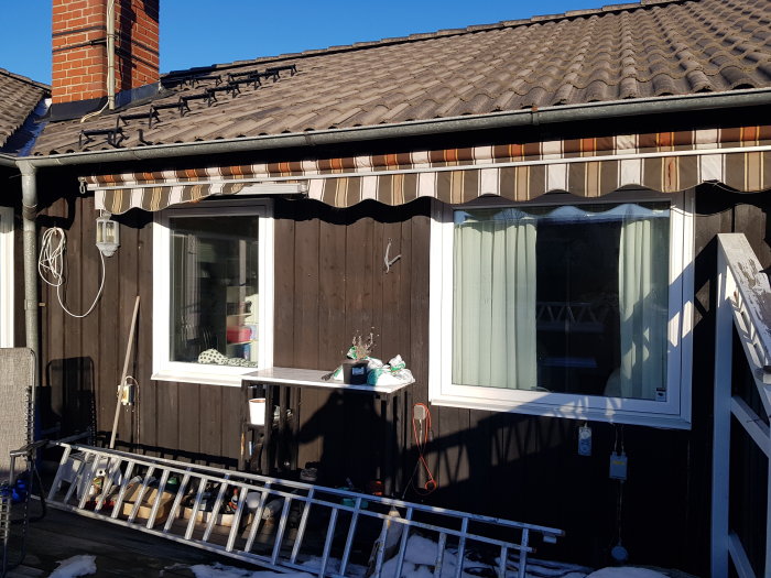 Ett brunt hus med veranda, markis, skor på räcket och snörest.