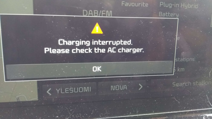 Bilens display visar felmeddelande: "Charging interrupted. Please check the AC charger", omgiven av damm och smuts.