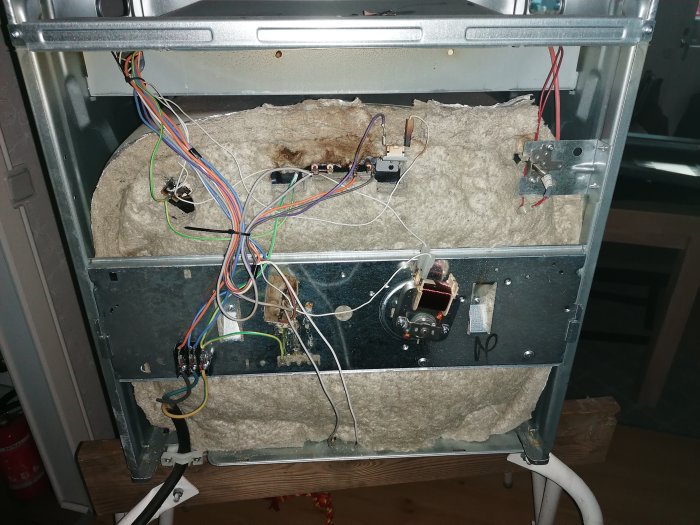 Öppnad, trasig elugn interiör med exponerade komponenter, sladdar och isolering. Behöver reparation eller utbyte.