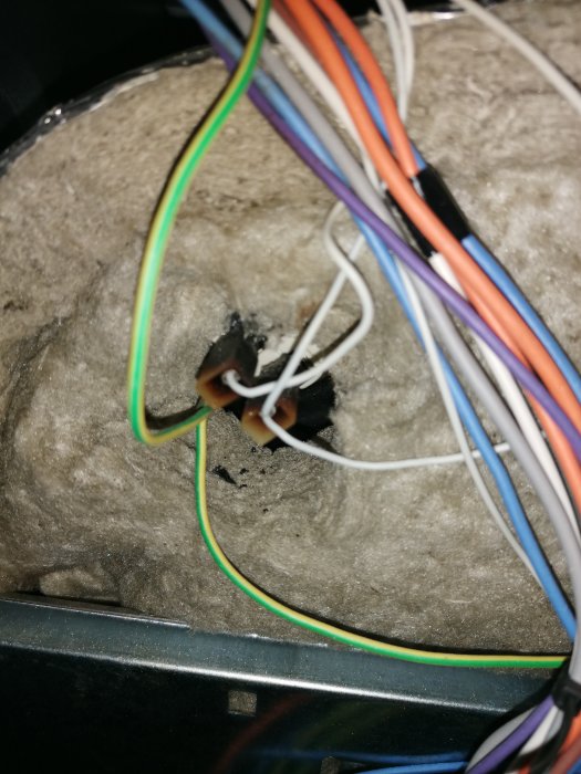 Ett trassel av färgglada kablar och eltejp ovanpå grå, luddig yta, med brända rester synliga.