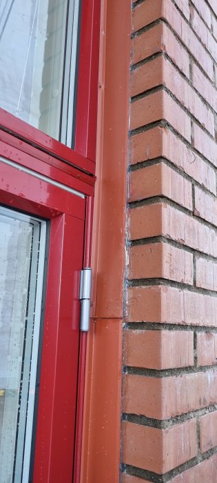 Röd fönsterkarm, tegelvägg, regndroppar, dagsljus, utomhus, vertikalt foto, byggnadsdetalj, fönsterhörn, arkitekturelement.