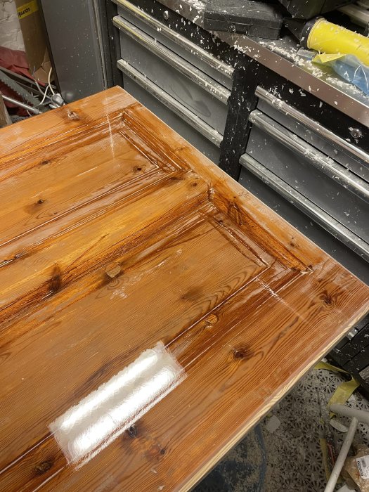 Träbord målas eller lackas, verktyg och målarföremål i bakgrunden, arbetsmiljö.