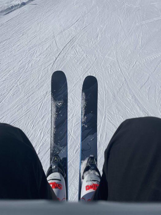 Person med skidor på snötäckt backe, klar för nedfart, vintersport, soligt väder.