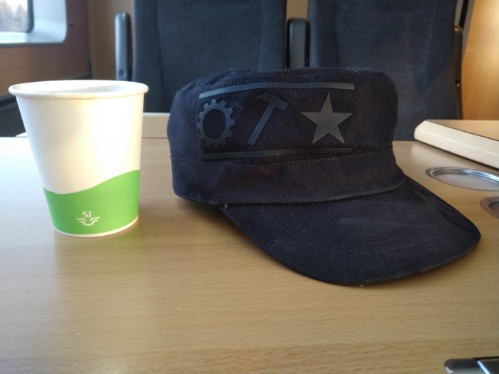 En kaffemugg och en keps på ett tågbord; symboler på kepsen, SJ-logga på muggen.