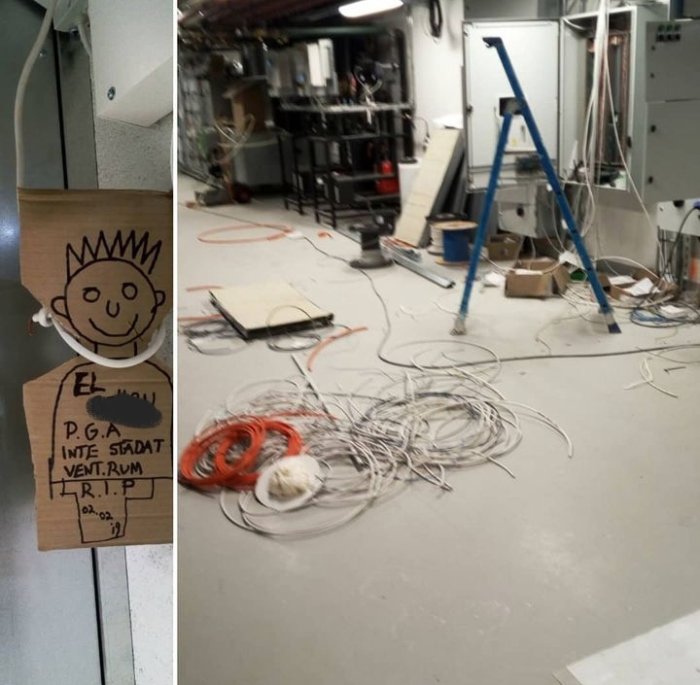 Oorganiserat teknikrum med kablar, stege, ritning på träskylt. Humoristisk "Vila i fred"-notering. Arbetsplats under konstruktion eller reparation.
