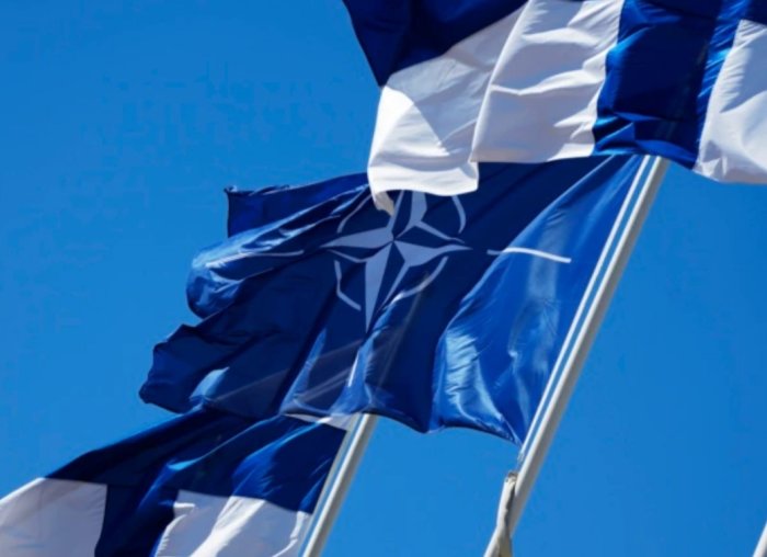 Fladdrande flaggor, blå och vit, NATO-symbol, mot klarblå himmel.