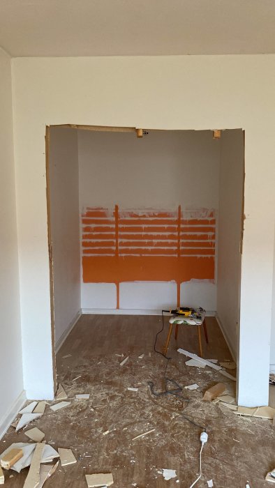 Ett rum under renovering med delvis rivna väggar och en målad sektion i orange.