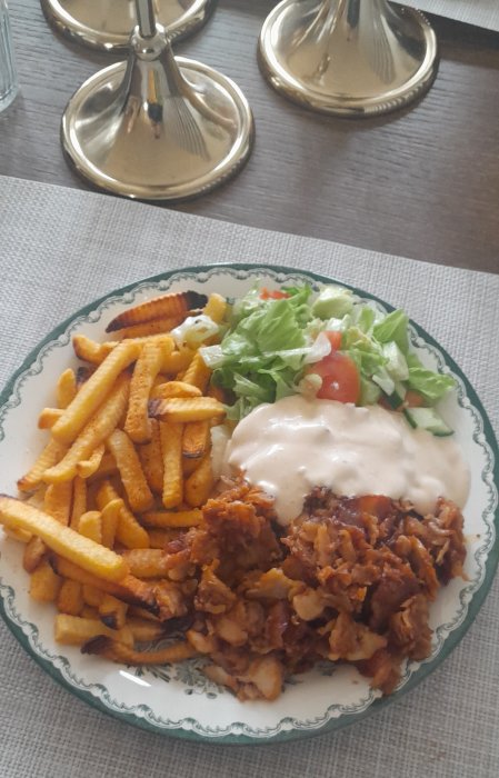 Tallrik med pommes frites, kebab, vit sås och sallad. Enkel dukning. Avslappnad måltid.