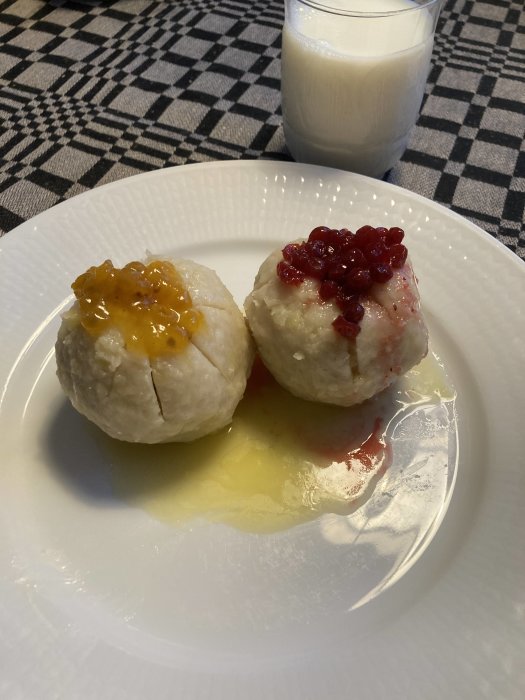 Två risgrynspuddingar med sylt, smält smör, på vit tallrik, rutig duk bakgrund, glas mjölk.