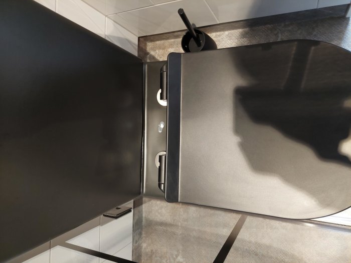 Svart ugn i kök med skuggor, toalettpapper och mobiltelefon synlig på golv.