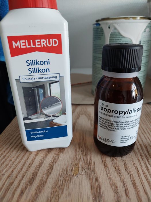 Två flaskor: silikonborttagningsmedel och isopropylalkohol på ett träbord, möjligen under rengöring eller renovering.