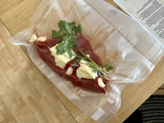 Rå köttbit med kryddor och smör, förberedd för sous-vide matlagning, på träskärbräda.