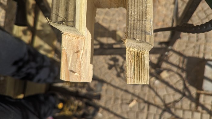Närbild på brutna träbitar i solljus med suddig bakgrund av stenläggning och personer.