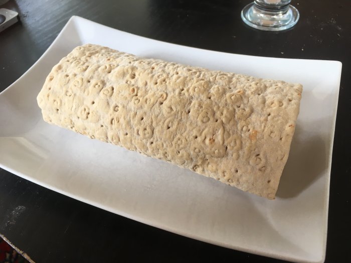 Ett stort, burrito-liknande, vikt knäckebröd på en vit långsträckt tallrik på ett bord.