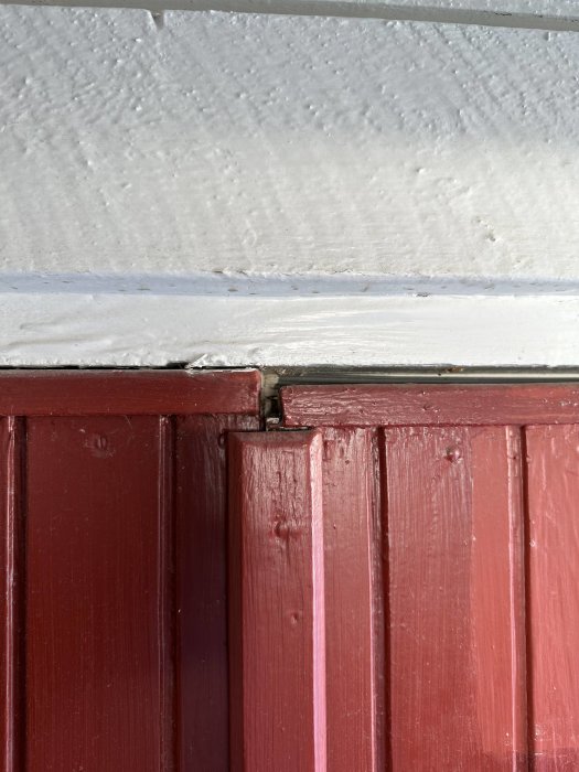 Vitstrukturell vägg ovanför rödmålad panel; sammansättningen visar tydligt slitage och färgskiftningar.