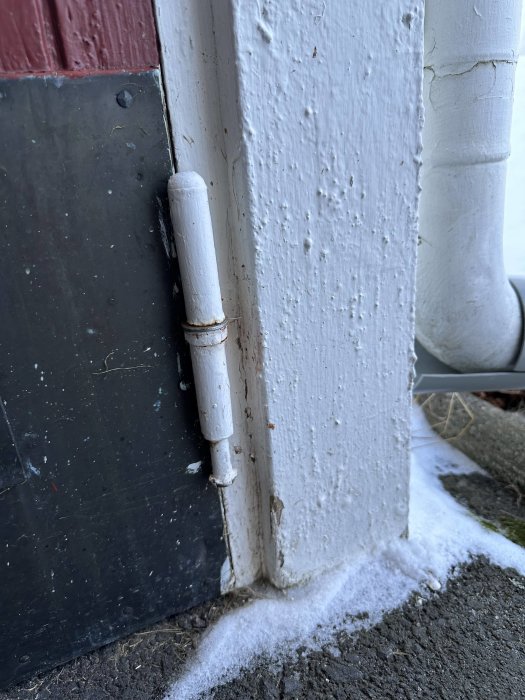 Dörr med gångjärn mot vit stolpe, nedslitet, rost, målarflagor, utomhus, smuts och lite snö.