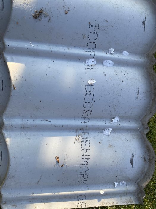 Grå metallisk yta med mönster av små hål och några spillror av is.