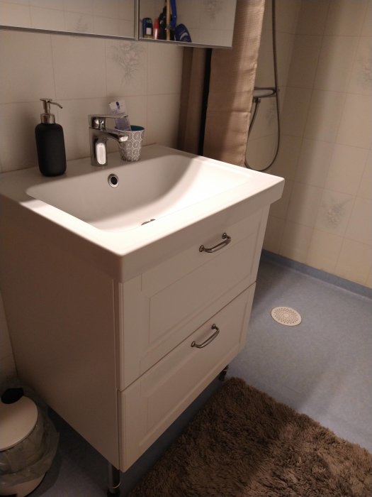 Ett badrum med handfat, spegel, duschdraperi, tvålpump och personliga hygienartiklar.