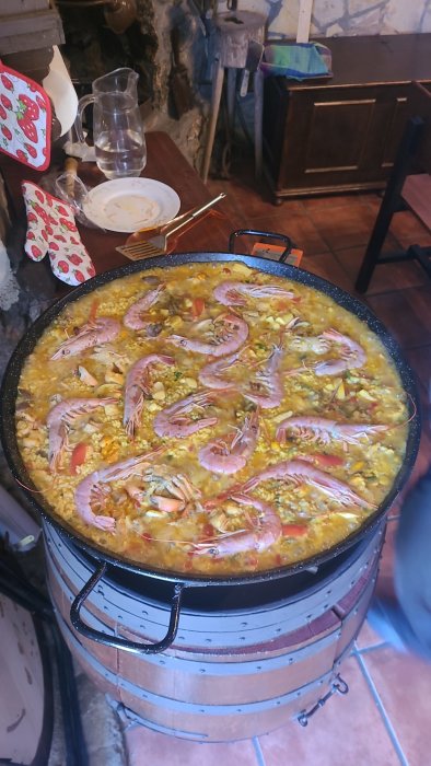 Stor paella i panna med skaldjur, grönsaker, på spis, rustik restaurangmiljö.