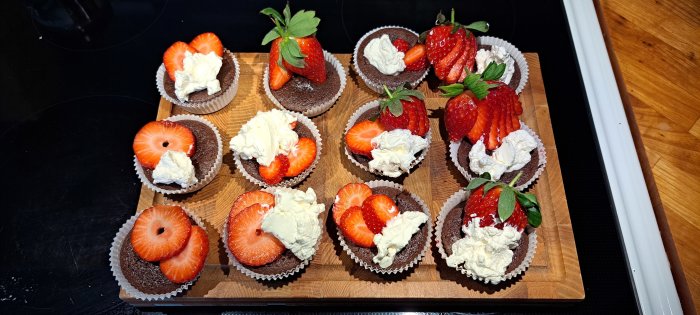 Chokladmuffins med grädde och jordgubbar på träbricka. Söta bakverk ordnade för servering.