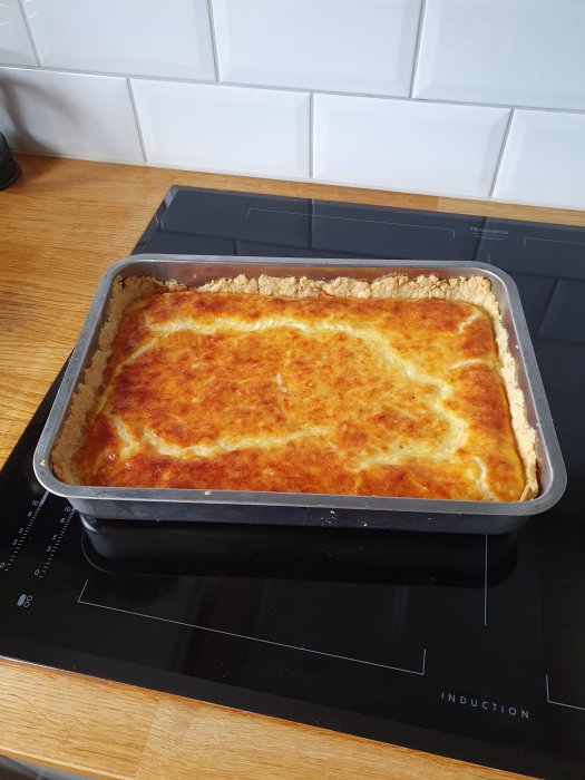Nygräddad, gyllene maträtt i ugnspanna på induktionshäll i modernt kök.