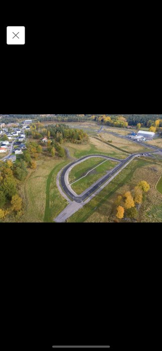 Flygbild över slingrande vägar och kringliggande landskap med träd i höstfärger och byggnader.