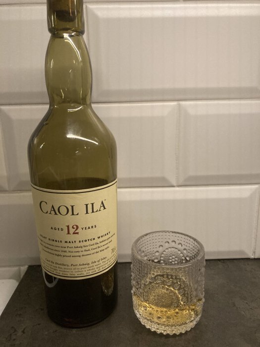 Flaska av Caol Ila 12 år gammal single malt scotch whisky, bredvid whiskyglas med dryck.