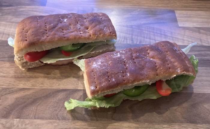 Två halvor av en sandwich med sallad, tomat och gurka på ett träbord.