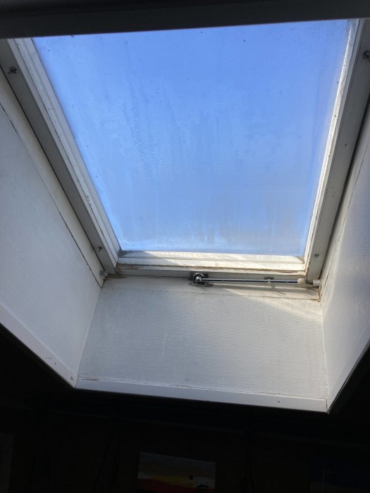 Taktakfönster med kondens, vitt fönsterfoder, dagsljus skiner igenom, ser inifrån ett rum.