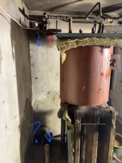 Äldre, korroderad varmvattenberedare i mörkt, slitet utrymme med synliga rör och indikationer märkta med färgade pilar.