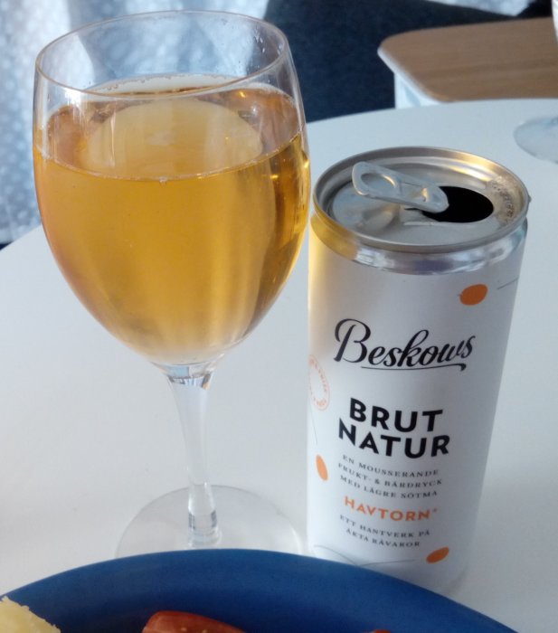 Ett glas med bubbel och en öppnad burk Brut Natur mousserande dryck på ett bord.