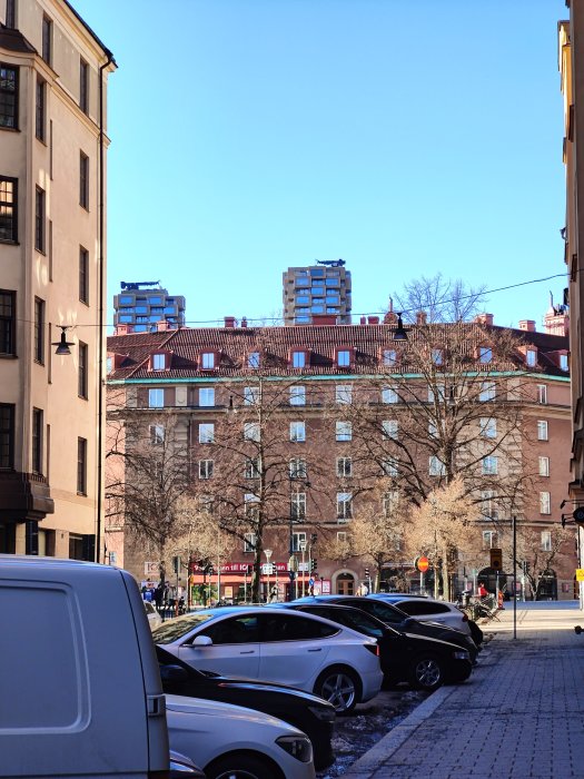 Stadsscen med byggnader, bilar, klar himmel och ingen snö på marken.