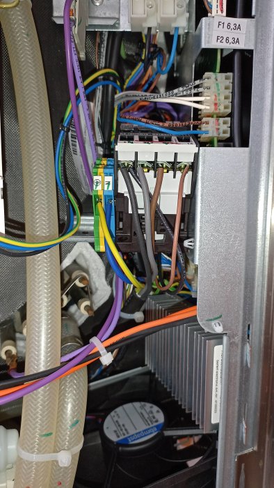 Bild inuti elektronisk apparat med färgkodade kablar, säkringar, anslutningar och kylfläns.
