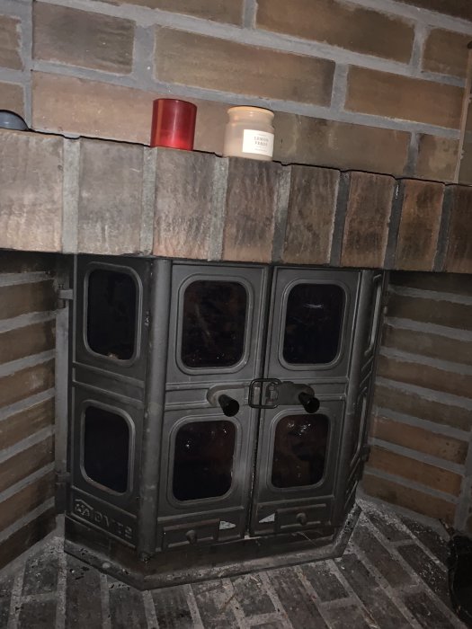 En kamin med svart yta, tegelvägg bakom, två ljus på övre hyllan.