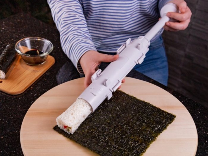 Person använder en sushi maker för att rulla sushi med noriblad på ett träskärbräde.