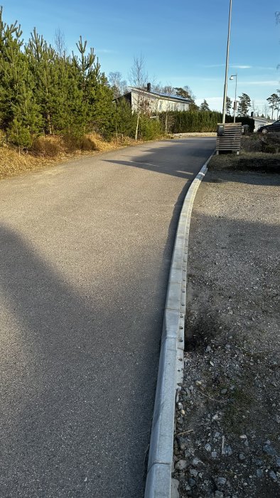 Asfalterad väg, kurva, kantsten, barrträd, villa, klar himmel, gatlyktor, utanför stad, dagtid.