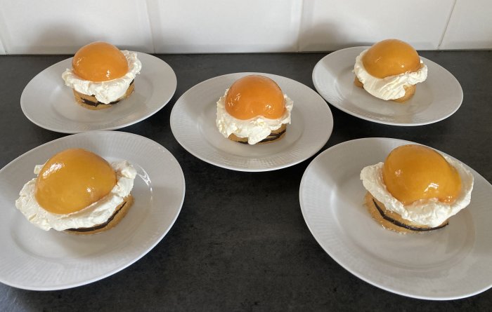 Fem desserttallrikar med liknande bakverk bestående av gräddskum och gul topping på mörk botten.