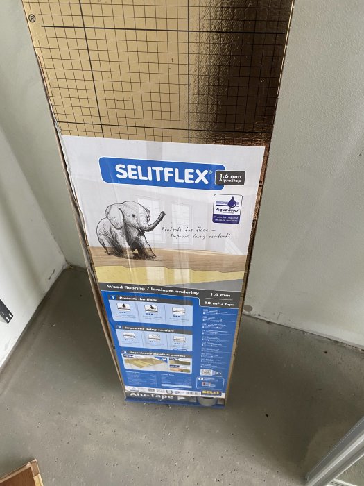 Paket med golvunderlägg märkt SELITFLEX, 1.6 mm tjock, med en elefantbild, i ett rum.