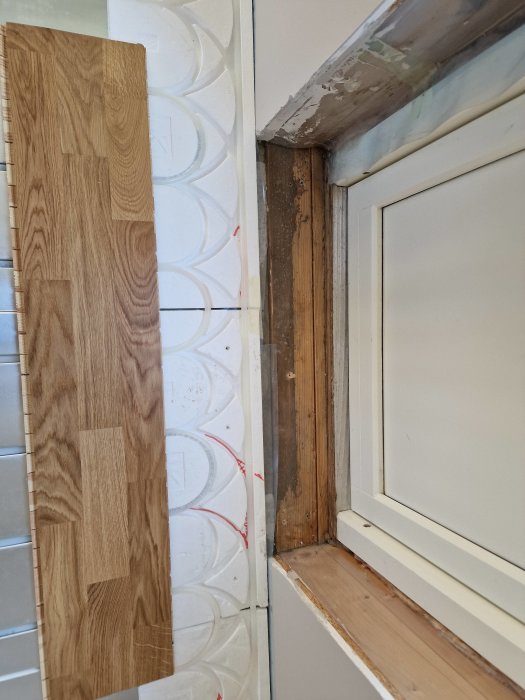 Pågående renovering, trägolv, bar väggyta, isolering, byggmaterial, fönster med vita karmar, ofärdigt byggprojekt.