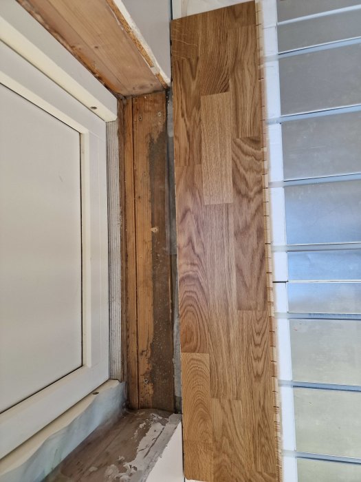 Fönsterrenovering, trägolvplanka, lister borttagna, synligt regelverk och isolering, oavslutat byggprojekt inomhus.