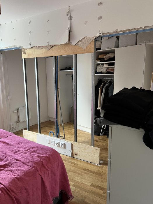 Sovrum under renovering med trästomme, droppskydd, säng och garderob synligt.